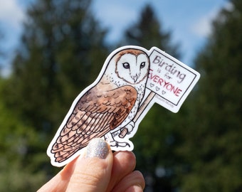 May include: A white and brown barn owl holding a sign that says "Birding is for everyone" with three red hearts. The owl is holding the sign with its right foot.