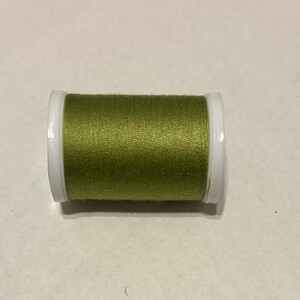 May include: A spool of olive green thread with white plastic sides. The thread is tightly wound around the spool, and the color is consistent throughout. This item is suitable for sewing and crafting projects.