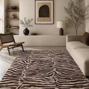 Op de afbeelding: Een rechthoekig vloerkleed met een herhalend zebrastreeppatroon in donkerbruin en crème. Het kleed ligt op een gladde vloer en toont een contrastrijk dierenprintontwerp dat het gehele oppervlak van de vloerbedekking beslaat.