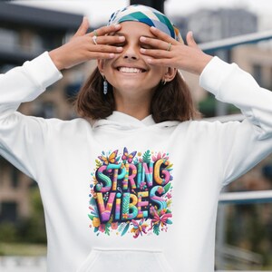Peut inclure: Un sweat à capuche blanc avec un motif coloré "SPRING VIBES". Le design présente des papillons, des fleurs et des feuilles dans des tons de bleu, rose, jaune et vert. Le sweat à capuche a une capuche à cordon et une poche avant.