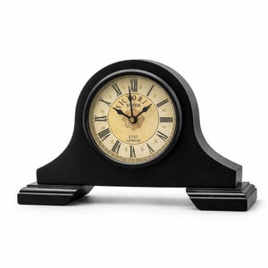 May include: A black mantel clock with a cream-coloured face featuring black Roman numerals and the text "VICTORI STATION" and "1747 LONDON" printed in the centre. The clock has a rounded top, a wide base, and black hour and minute hands.
