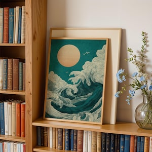 K&ouml;nnte beinhalten: Ein gerahmter Kunstdruck, der eine stilisierte Meereslandschaft mit einer gro&szlig;en Sonne und tosenden Wellen in T&uuml;rkis, Wei&szlig; und Dunkelblau zeigt. Das Kunstwerk wird auf einem Holzregal mit einem B&uuml;cherregal und einer Vase mit blauen Blumen ausgestellt.