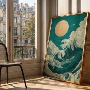 K&ouml;nnte beinhalten: Ein gerahmter Kunstdruck, der eine stilisierte Ozeanszene mit einer gro&szlig;en Sonne und tosenden Wellen darstellt. Das Kunstwerk zeigt Farbt&ouml;ne von T&uuml;rkis, Blau und Creme mit einem goldenen Rahmen. Der Druck lehnt an einer Wand in der N&auml;he eines Fensters.