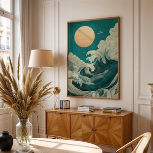 K&ouml;nnte beinhalten: Ein gerahmter Kunstdruck, der eine stilisierte Ozeanszene mit einer gro&szlig;en goldenen Sonne und brechenden Wellen in T&uuml;rkis- und Wei&szlig;t&ouml;nen zeigt. Das Kunstwerk wird &uuml;ber einem Holzschrank in einem hellen Raum ausgestellt.