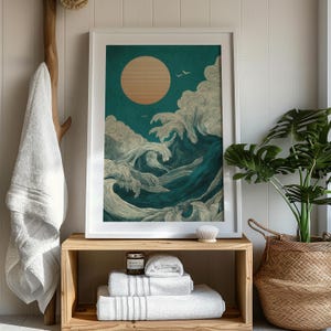 K&ouml;nnte beinhalten: Gerahmter Kunstdruck mit stilisierten Meereswellen in T&uuml;rkis und Wei&szlig;, mit einer gro&szlig;en, strukturierten Sonne. Zwei V&ouml;gel fliegen &uuml;ber den Wellen. Der Druck steht auf einem Holzregal mit gefalteten wei&szlig;en Handt&uuml;chern und einer Kerze.