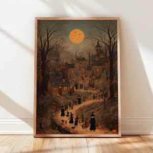 May include: A framed vertical art print depicting a nighttime village scene under a large orange full moon. Figures in pointed hats and dark cloaks walk along a winding path lined with glowing orange pumpkins among stone cottages and bare trees.