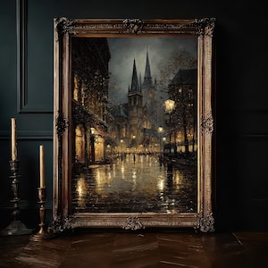 May include: A framed oil painting depicting a rainy European city street at night with glowing street lamps, dark buildings, and a tall church spire in the background. The artwork is encased in an ornate, dark bronze-coloured vintage frame.
