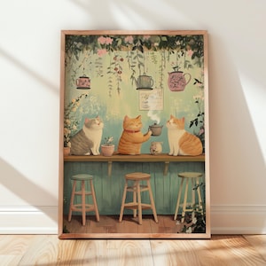 Può includere: Una stampa artistica incorniciata raffigurante tre gatti seduti a un bancone di legno in un giardino. I gatti sono grigi e arancioni, con un gatto arancione che tiene in mano una piccola teiera. Teiere appese e viti verdi decorano lo sfondo.