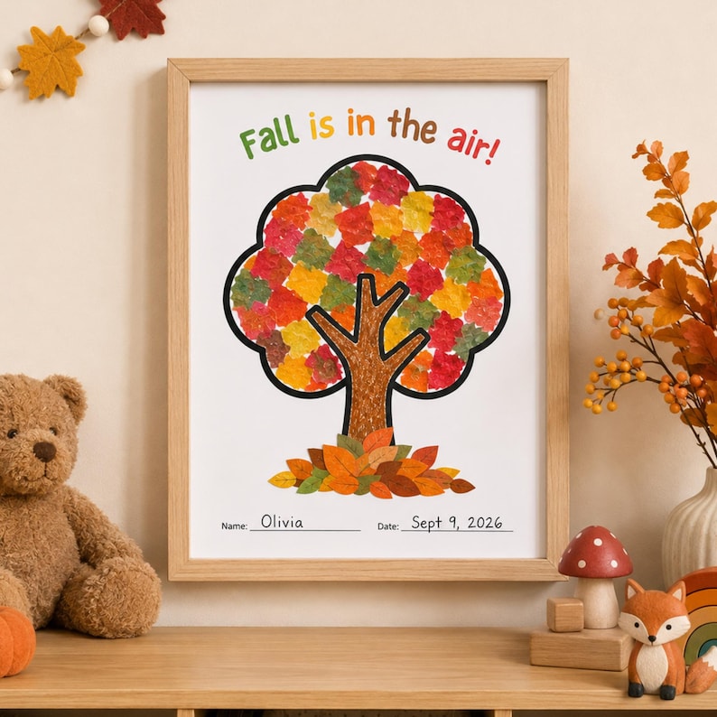 May include: A framed art print featuring a tree illustration with colorful leaf-shaped cutouts in red, orange, yellow, and green. The text reads Fall is in the air! with Name: Olivia and Date: Sept 9, 2026 printed at the bottom of the white paper.