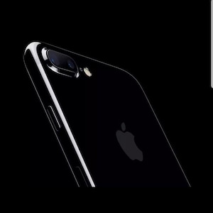 Puede incluir: Un smartphone negro brillante visto desde un ángulo posterior. El dispositivo cuenta con un módulo de cámara de doble lente en la esquina superior, un pequeño flash circular y un logotipo de Apple centrado. El perfil lateral muestra un botón de volumen.