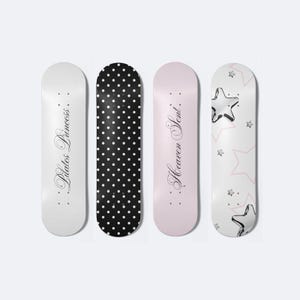May include: Four decorative skateboards. One is white with the text "Pilates Princess". Another is black with white polka dots. The third is pink with the text "Heaven Sent". The last is white with pink stars.