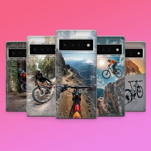 Op de afbeelding: Een verzameling telefoonhoesjes met mountainbike-scènes. Elke hoes toont een andere afbeelding van fietsers op paden, met verschillende landschappen, waaronder bossen, bergen en een fietser in de lucht. De hoesjes hebben een zilveren frame en een roze achtergrond.