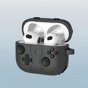 Pode incluir: Uma capa protetora preta e cinza para fones de ouvido sem fio, projetada para se assemelhar a um controle de videogame. A capa está aberta, revelando fones de ouvido brancos. O design do controle inclui botões direcionais e botões de ação coloridos.