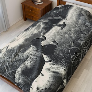 May include: Monochrome blanket depicting a hunting scene with two dogs and birds in flight. The detailed illustration shows dogs in a field of tall grass, with a cloudy sky backdrop. The blanket is displayed on a wooden bed frame.