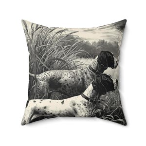 Könnte beinhalten: Quadratisches Kissen mit einer Schwarz-Weiß-Illustration von zwei Jagdhunden in einem Feld mit hohem Gras. Die Hunde haben schwarz-weiß geflecktes Fell und tragen Halsbänder. Der Hintergrund zeigt einen bewölkten Himmel und Bäume.