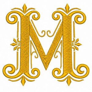 Può includere: Una lettera M ricamata in giallo dorato con volute complesse e decorazioni ornamentali sulla parte superiore e inferiore. Il design presenta un motivo a punto strutturato su tutta la lettera e sugli abbellimenti circostanti.
