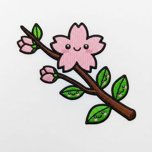 May include: Embroidered patch of a smiling pink cherry blossom on a brown stem with green leaves. The leaves and flower have smiling faces. The patch is on a white background.