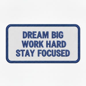 Puede incluir: Parche bordado con las palabras "DREAM BIG WORK HARD STAY FOCUSED" en azul sobre fondo blanco. El parche tiene un borde azul y forma rectangular.