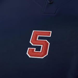 May include: A navy blue baseball jersey featuring a large, embroidered number 5 in red with a white border. The jersey has a button-down collar.