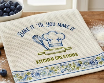 May include: Off-white waffle-weave kitchen towel with the text "Bake it 'til you make it" in blue script. A chef's hat, whisk, and rolling pin are also in blue and green. The bottom border has a blue floral design. The words "Kitchen Creations" are in green.