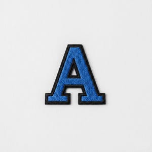 Puede incluir: Parche bordado azul con borde negro con la letra "A". La letra está en una fuente audaz de estilo universitario, sobre un fondo blanco. Este parche es adecuado para personalizar prendas.
