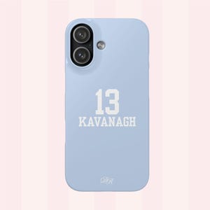 Puede incluir: Funda de teléfono azul claro con una abertura para una cámara de doble lente. La funda presenta el número "13" y el nombre "KAVANAGH" en letras blancas. Las iniciales "DR" están en la parte inferior. Funda para smartphone.