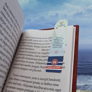 Op de afbeelding: Een rechthoekige boekenlegger met afgeronde bovenranden, voorzien van een lichtblauw bovengedeelte met een ijshockeystick-icoon en hartje, de tekst "SOMETIMES PEOPLE SNEAK UP ON YOU AND SUDDENLY YOU DON'T KNOW HOW YOU EVER LIVED WITHOUT THEM" en een marineblauwe basis met het nummer 44 en de tekst "THE DEAL - OFF CAMPUS".