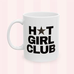 Könnte beinhalten: Weiße Keramik-Tasse mit dem Text "HOT GIRL CLUB" in schwarzen Blockbuchstaben. Der Stern im Wort "HOT" hat ein Leopardenmuster. Die Tasse hat einen weißen Henkel und steht vor einem rosa Hintergrund.