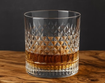 May include: A clear, diamond-cut glass filled with amber liquid, likely whiskey or bourbon. The glass sits on a wooden surface, with a dark background. The glass has a thick base and a textured pattern.