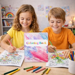Peut inclure: Deux enfants colorient à une table, avec un livre de coloriage à spirale au centre. La couverture du livre présente un motif aquarelle et les mots "Coloring Book". Des crayons de couleur sont éparpillés sur la table, et les enfants sourient en coloriant.