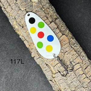 May include: White fishing lure with a colorful polka dot pattern, including black, green, red, blue, and yellow dots. The lure has a double hook and the text "117L".