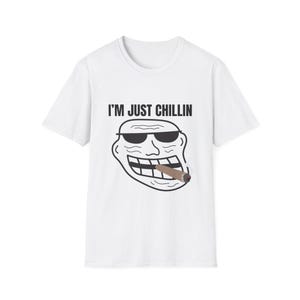 Puede incluir: Camiseta blanca con el texto "I'M JUST CHILLIN" sobre una cara de dibujos animados con gafas de sol y fumando un cigarro. El gráfico es en blanco y negro, con el cigarro en tonos marrones.