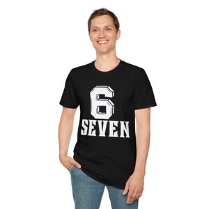 Puede incluir: Camiseta negra con el número 6 y la palabra SEVEN en letras blancas. El número 6 tiene un contorno blanco. La persona lleva vaqueros azules.