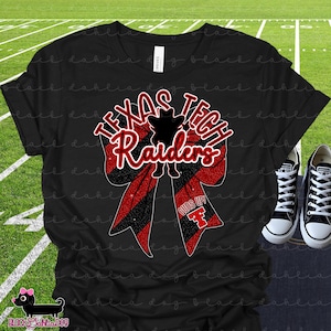 Könnte beinhalten: Ein schwarzes T-Shirt mit einer großen Grafik einer rot-schwarzen Glitzer-Haarschleife. Das Design enthält den Text "TEXAS TECH Raiders" in Weiß und Rot, eine Maskottchen-Silhouette und den Text "GUNS UP!" mit einem roten "TT"-Logo.