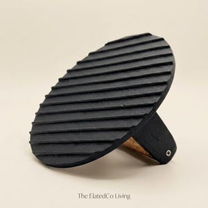 May include: Black wooden meat press with a grooved oval pressing surface and a small wooden handle. The ElatedCo Living is printed at the bottom.