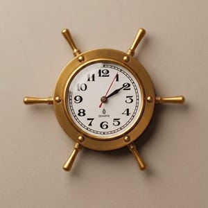 May include: A brass-toned wall clock shaped like a ship's wheel. The clock features a white face with black Arabic numerals, black hour and minute hands, and a thin red second hand. The word QUARTZ is printed in black below the center hands.