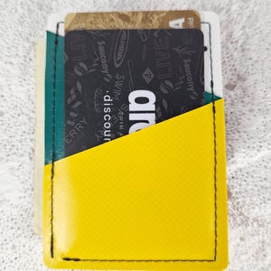 May include: A yellow and green cardholder with black stitching. The cardholder has a diagonal pocket and contains several cards with text and logos. The cardholder is made of a textured material.