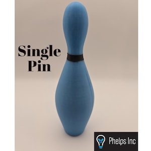 Puede incluir: Un bollo de bolos azul claro con una banda negra alrededor del cuello. El texto "Single Pin" está impreso en el lado izquierdo del bollo. El logotipo de Phelps Inc. está en la esquina inferior derecha.