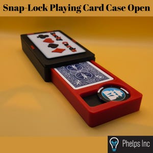 Può includere: Un astuccio per carte da gioco nero e rosso con chiusura a scatto in posizione aperta. Il coperchio presenta la scritta "Jacky Cards" con simboli di semi. All'interno, un mazzo di carte con dorso blu è visibile accanto a una fiches circolare.