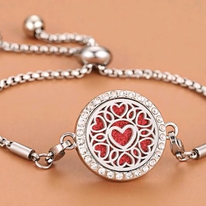 Peut inclure: Bracelet argenté avec un pendentif rond orné d'un motif de cœur rouge. Le pendentif est entouré de cristaux transparents et d'un motif ajouré décoratif. Le bracelet est de type chaîne et possède une fermeture réglable.