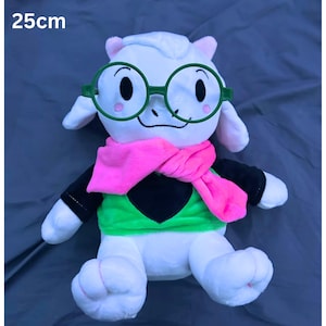 May include: A plush toy character, approximately 9.8 inches tall, with white fur, pink ears, and a pink scarf. The character wears green glasses and a green and black outfit. The text "25cm" is visible in the image.