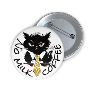 Puede incluir: Un botón blanco con un gato negro gruñón con una corbata a rayas amarillas y blancas y una camisa blanca. El texto "NO MILK COFFEE" está escrito alrededor del gato. Un segundo botón plateado es visible.