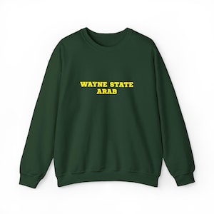 May include: A dark forest green crewneck sweatshirt featuring the text WAYNE STATE ARAB printed in bold yellow capital letters across the center of the chest. The garment has long sleeves, a ribbed neckline, and ribbed cuffs at the wrists and waist.