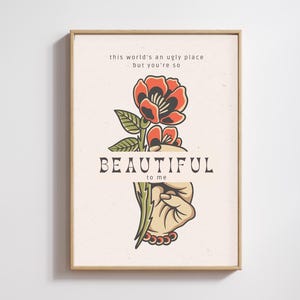 May include: Framed art print with a tattoo-style floral design. The image shows a red and black flower held by a hand, with the text "BEAUTIFUL to me" and the quote "this world's an ugly place - but you're so".
