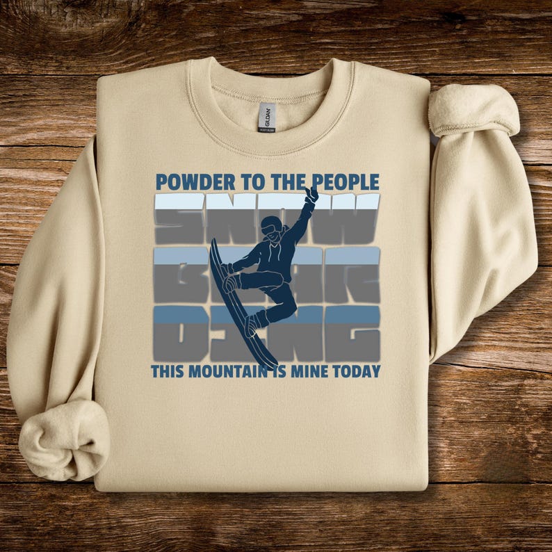 May include: Beige sweatshirt with the text "POWDER TO THE PEOPLE" and "SNOW BOARDING". A blue graphic of a snowboarder is in the center. The text "THIS MOUNTAIN IS MINE TODAY" is below the graphic.