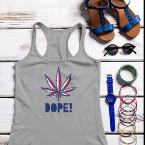 Op de afbeelding: Een grijze tanktop met een cannabisbladontwerp in rood, wit en blauw, met het woord "DOPE!" in blauw. De afbeelding bevat ook blauwe sandalen, zonnebrillen, een blauw horloge en armbanden.