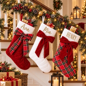 May include: Three personalized Christmas stockings hanging in a row. The first is red with a plaid bow, the second is white with a red velvet bow, and the third is plaid with a red velvet bow. Each features embroidered names Ava, Mia, and Henry.