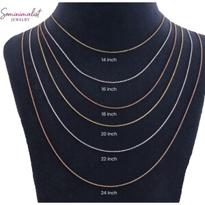 May include: A display of six delicate necklaces in varying lengths, ranging from 35.5 cm to 61 cm. The necklaces are gold, silver, and rose gold, showcasing different chain styles. The lengths are labeled on the display. The brand name "Sominimalist Jewelry" is visible.