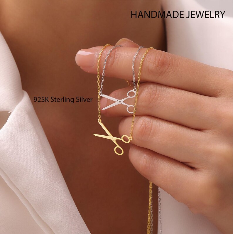 May include: Two necklaces with scissor pendants, one gold-toned and one silver-toned. The chains are delicate, and the pendants are detailed. The image includes the text "HANDMADE JEWELRY" and "925K Sterling Silver".