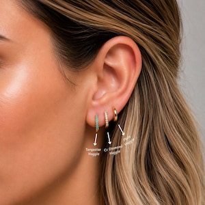 May include: A close-up of three gold hoop earrings. One earring is turquoise, one is encrusted with small clear stones, and the third is a plain gold hoop. The earrings are labeled "Turquoise Huggie", "Cz Diamond Huggie", and "Plain Huggie".